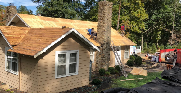 a couple of men working on the roof of a house.